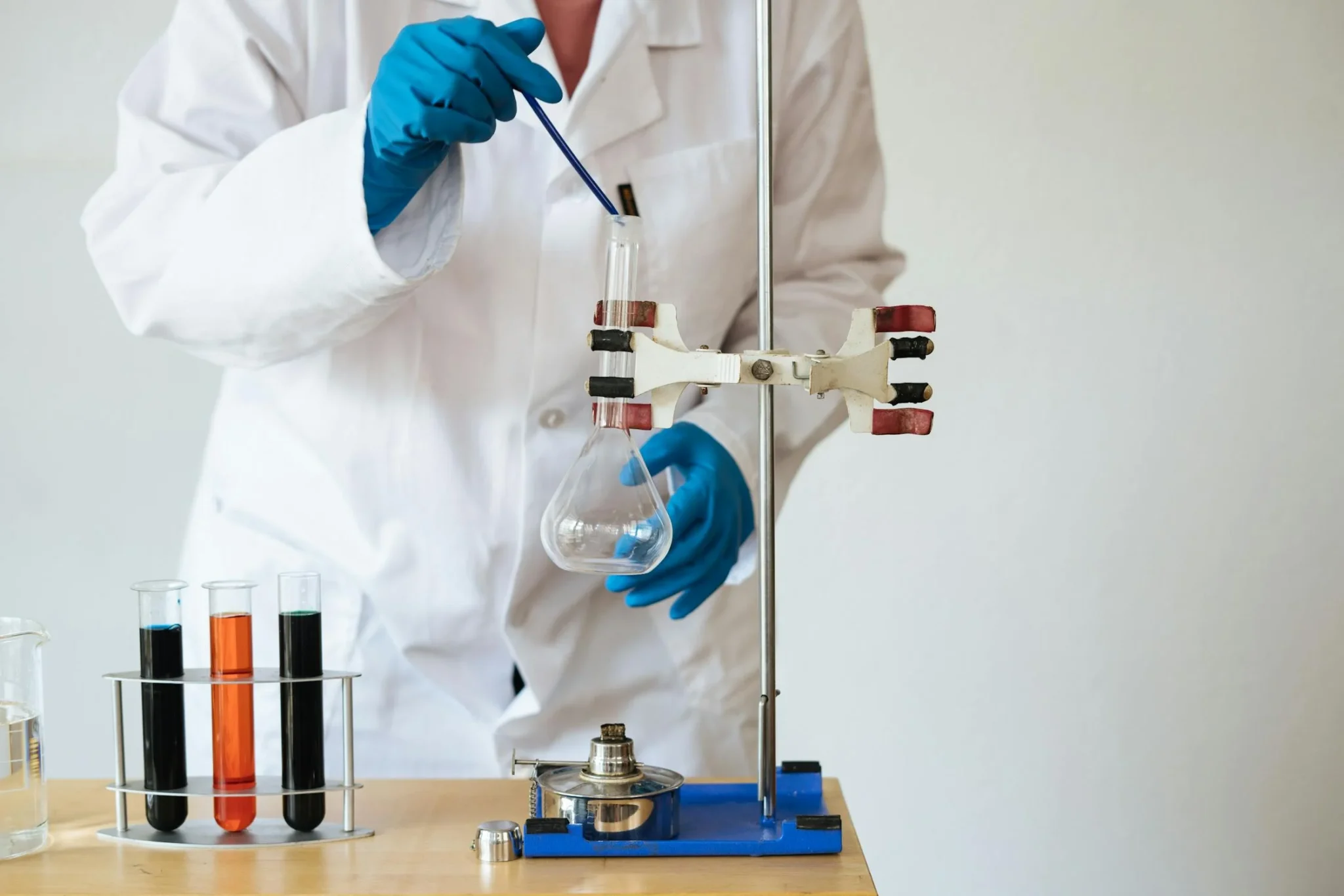 A student in a lab coat and gloves holding a test tube, conducting experiments for medicinal and pharmaceutical chemistry homework